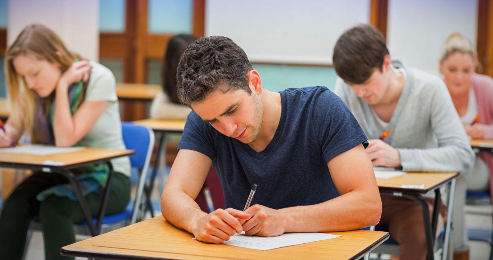 在教室里，穿着便服的两名白人学生坐在课桌前，像考试一样在纸上写字.